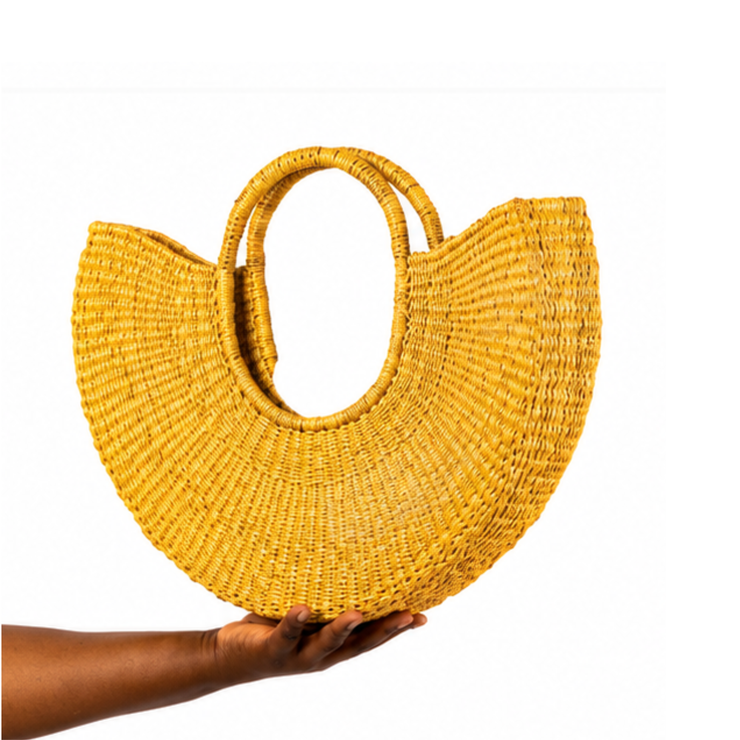A yellow woven straw half-moon tote bag with a large oval cutout handle, held up by a person's hand against a plain white background.