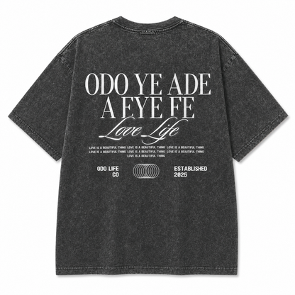 A dark gray mineral-wash t-shirt shown from the back, featuring a large white graphic print with the text 'ODO YE ADE A EYE FE Love Life' and smaller text below.