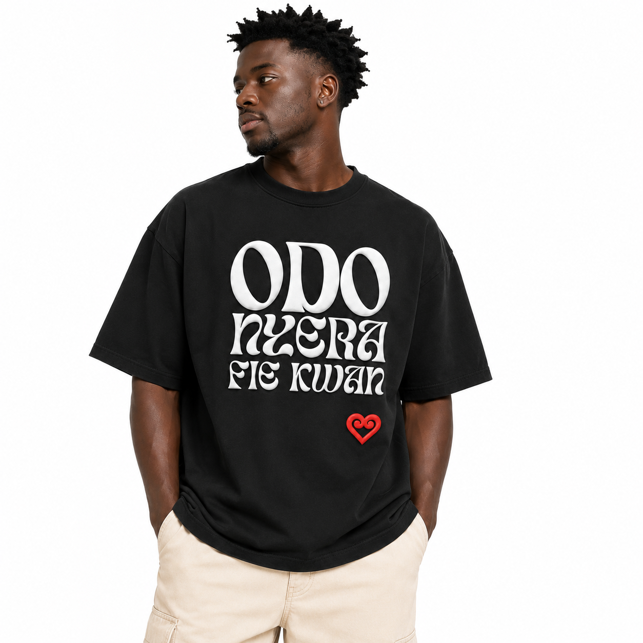 A man wearing a black t-shirt with white text reading 'ODO NYERA FIE KWAN' and a small red heart logo, paired with beige shorts, against a plain white background.