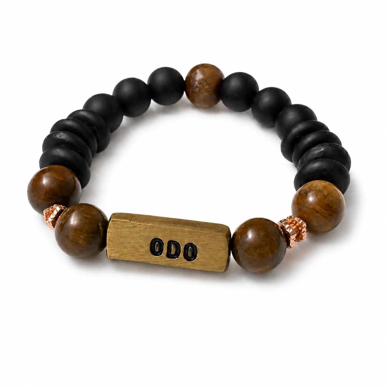 A beaded stretch bracelet featuring matte black beads, polished brown tiger's eye beads, a rectangular engraved wooden nameplate spelling 'ODO', and small rose gold spacer beads, shown on a white background.