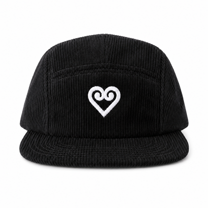 A black corduroy 5-panel cap with a white embroidered heart logo on the front, set against a plain white background.