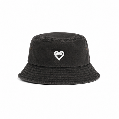 A washed black bucket hat featuring a small white embroidered heart with a spiral design on the front, set against a plain white background.