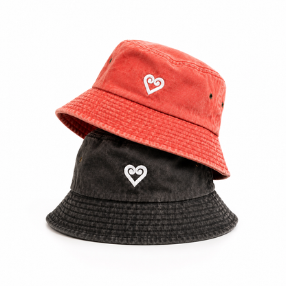 Two bucket hats stacked on a white background, one in coral red and one in washed black, both featuring a white heart outline logo on the front.