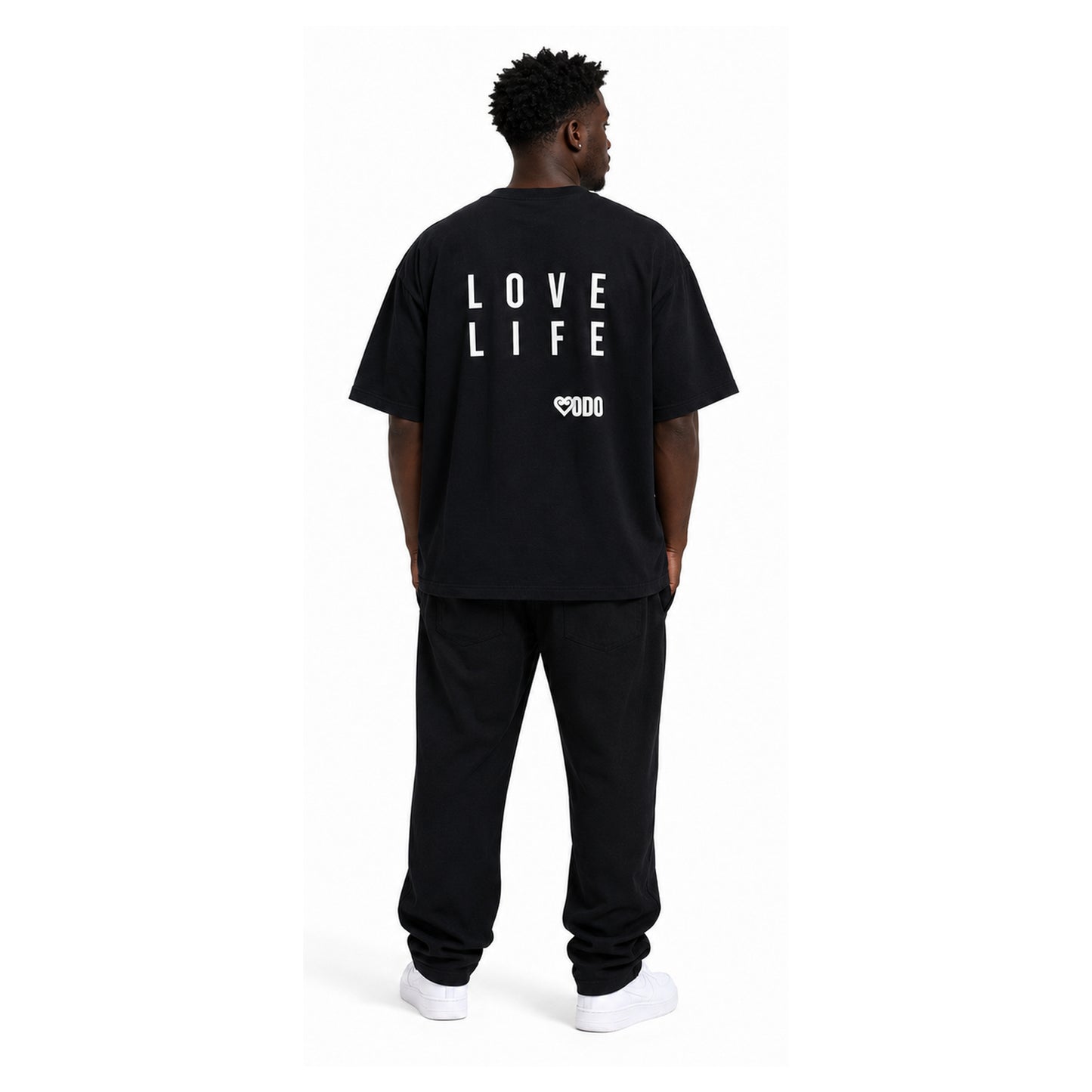 A man viewed from behind wearing a black oversized t-shirt with 'LOVE LIFE' printed in white block letters on the back, paired with black sweatpants and white sneakers, against a plain white background.