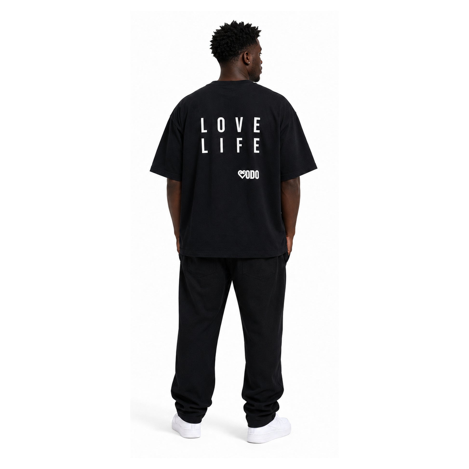 A man viewed from behind wearing a black oversized t-shirt with 'LOVE LIFE' printed in white block letters on the back, paired with black sweatpants and white sneakers, against a plain white background.