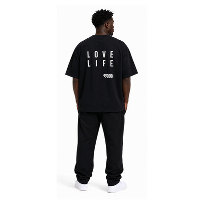 A man viewed from behind wearing a black oversized t-shirt with 'LOVE LIFE' printed in white block letters on the back, paired with black sweatpants and white sneakers, against a plain white background.