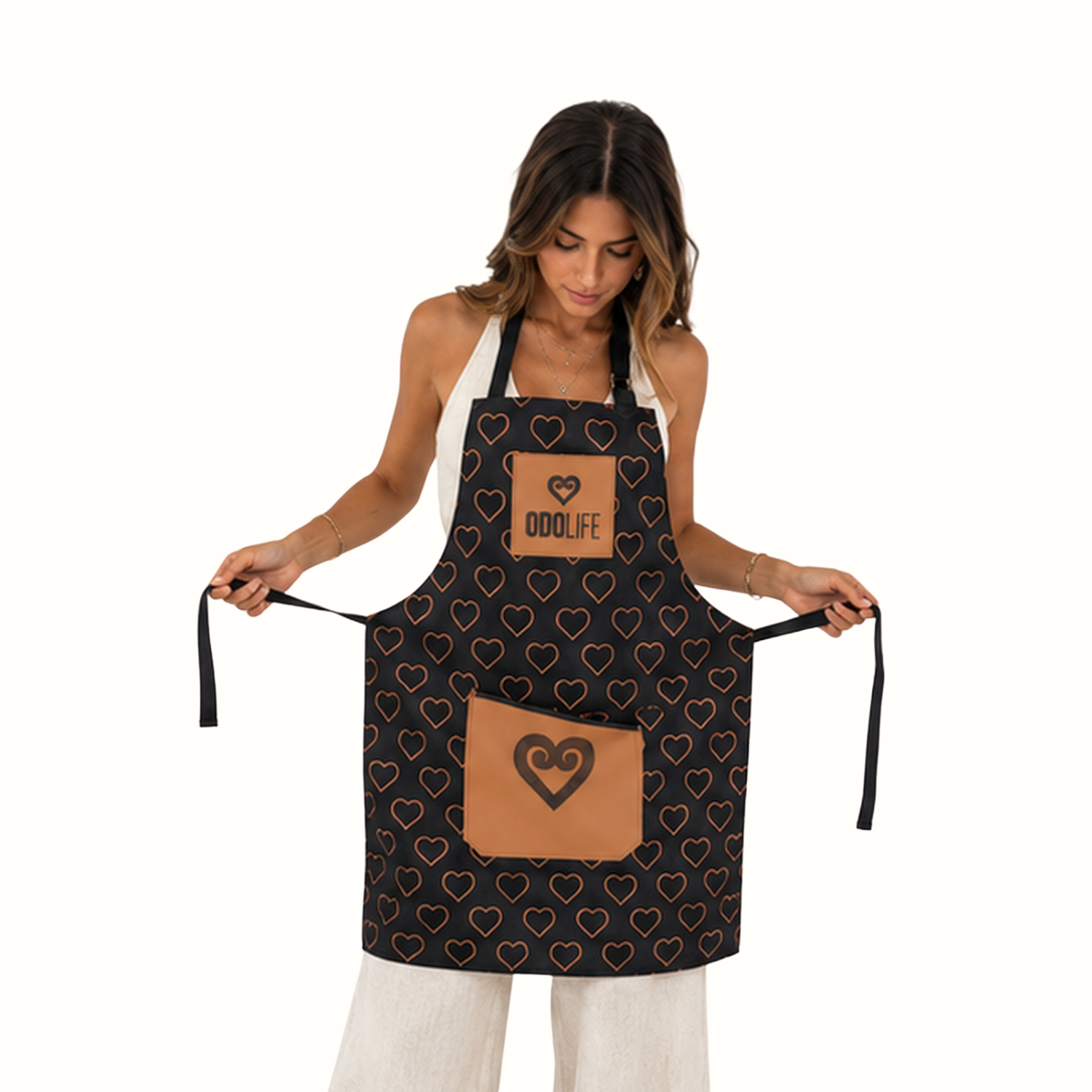 A woman modeling a black apron with a repeating heart pattern and two tan patches, one on the chest and one on the front pocket. The chest patch is printed with the brand name 'ODOLIFE'.