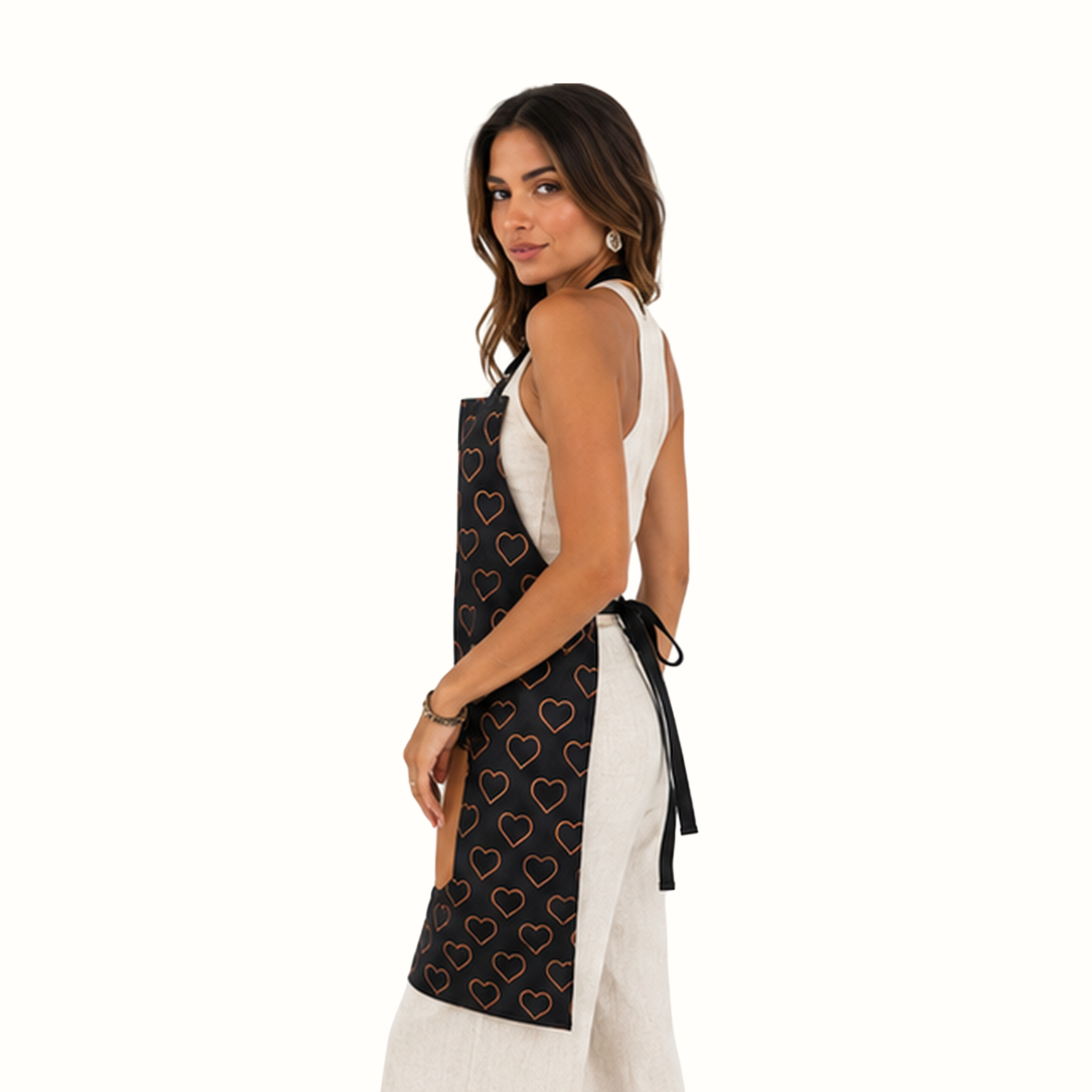 A woman wearing a black apron with a pattern of outlined red and orange hearts, styled over a white sleeveless dress against a plain white background.