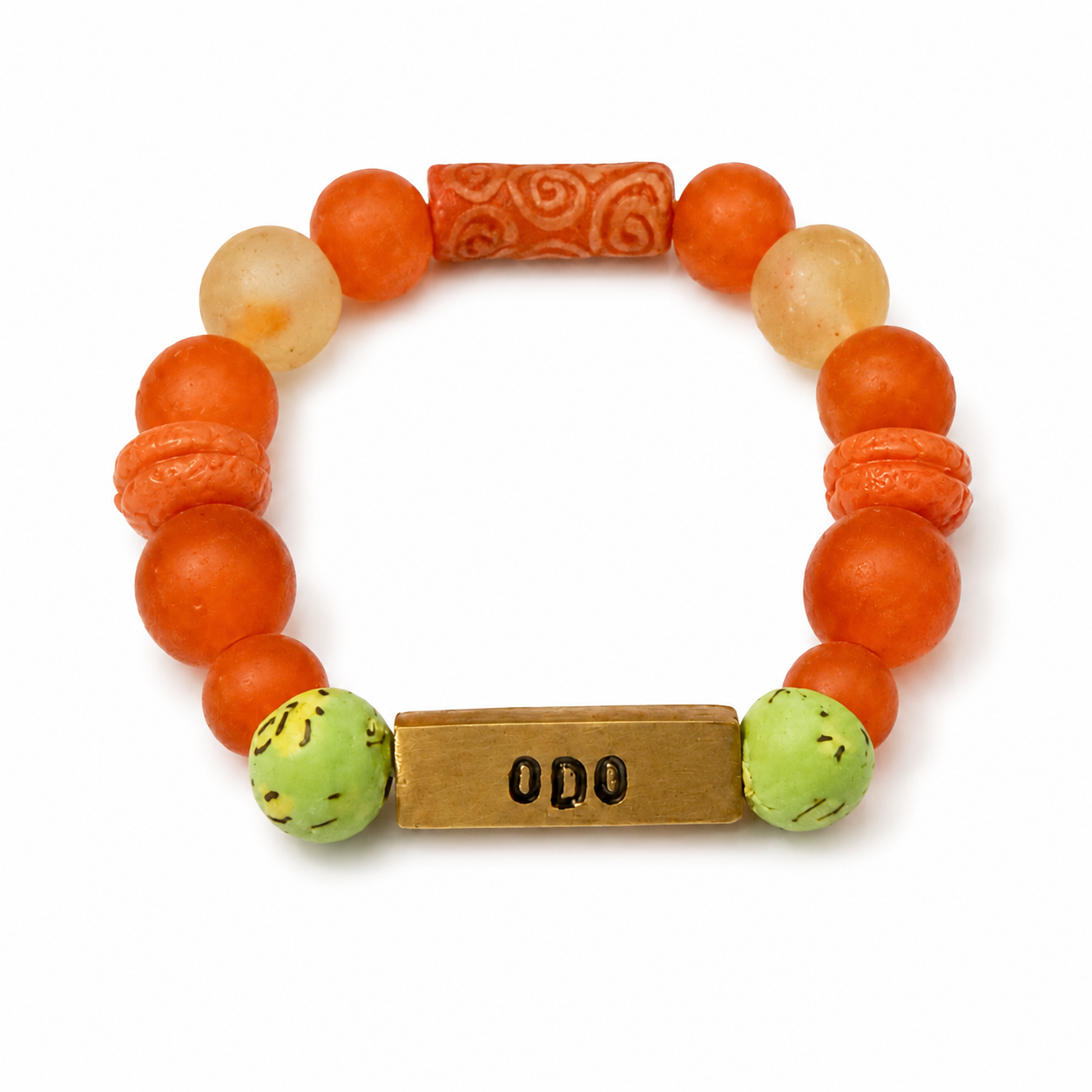 A beaded stretch bracelet featuring round orange and peach beads, a carved orange cylindrical bead, two light beige stone beads, two green marbled beads, and a rectangular gold-toned metal charm engraved with 'ODO'.
