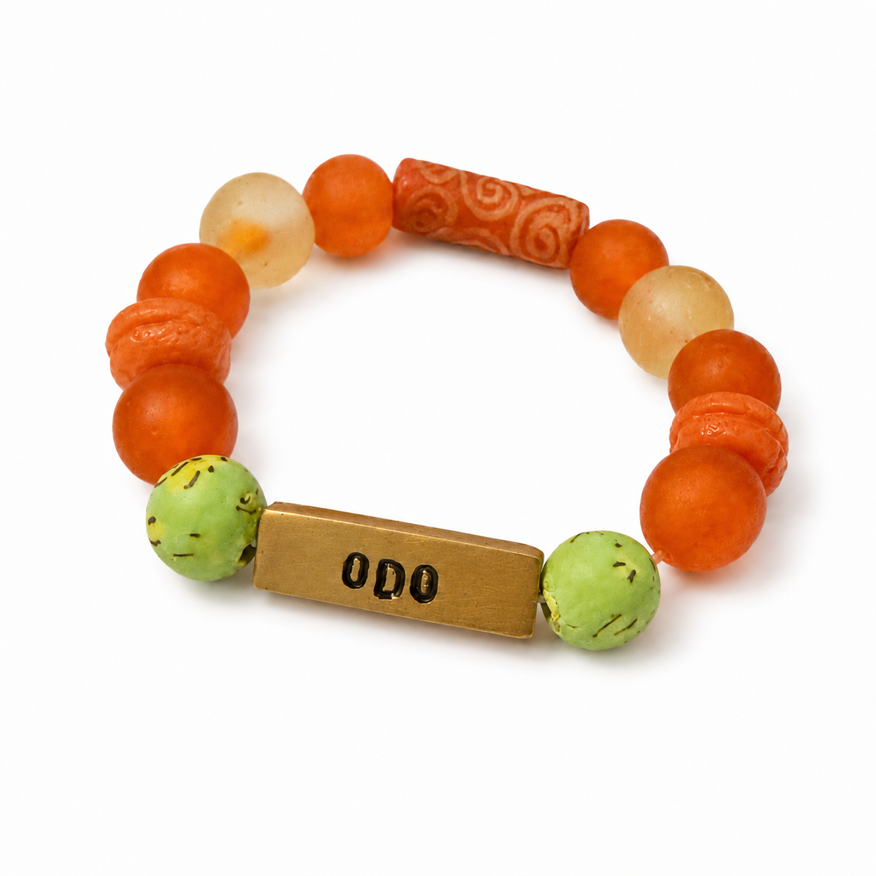 A beaded stretch bracelet featuring orange and light orange beads, a carved orange cylinder, two light green beads with black speckles, and a rectangular gold-toned metal charm engraved with 'ODO'.