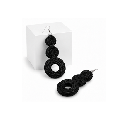 Raffia black braided drop earrings with three stacked spiral rings and silver fishhook wires, displayed on a white cube and a white surface.