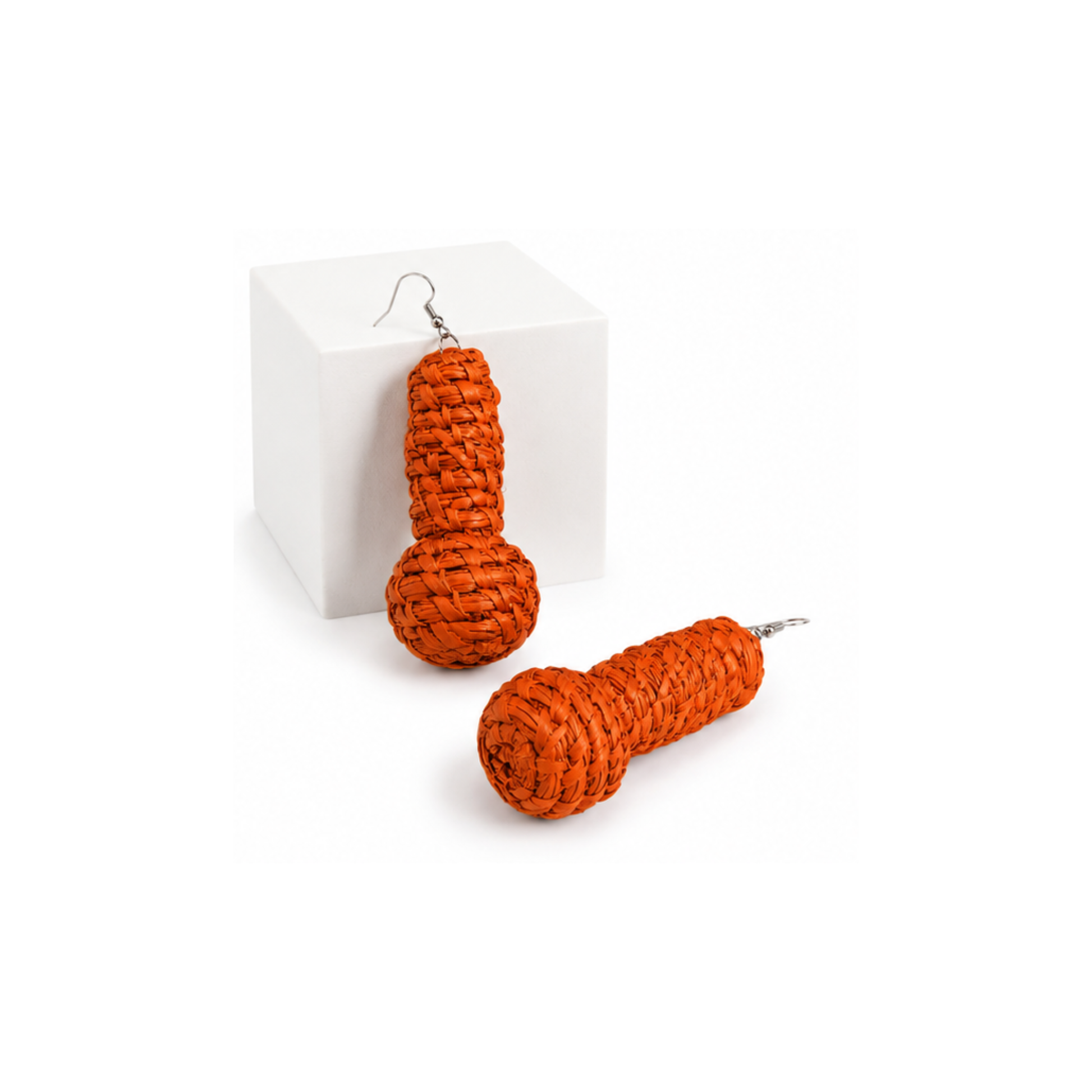 A pair of orange braided raffia novelty earrings with silver fishhook wires, displayed on a white cube and a white surface.